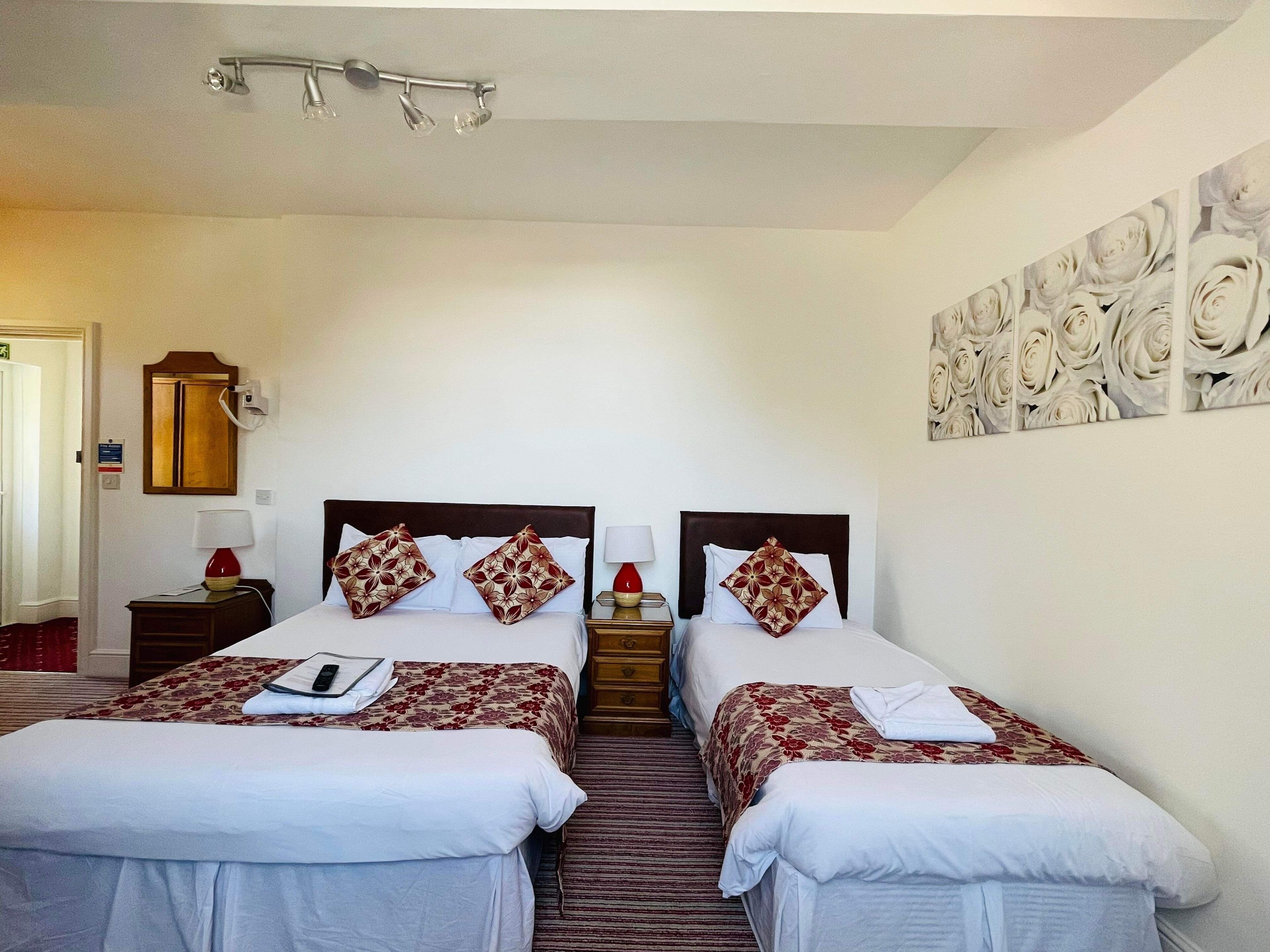 Habitación de hotel con dos camas, una mesita de noche con lámpara, una lámpara de pared y una obra de arte floral en la pared.