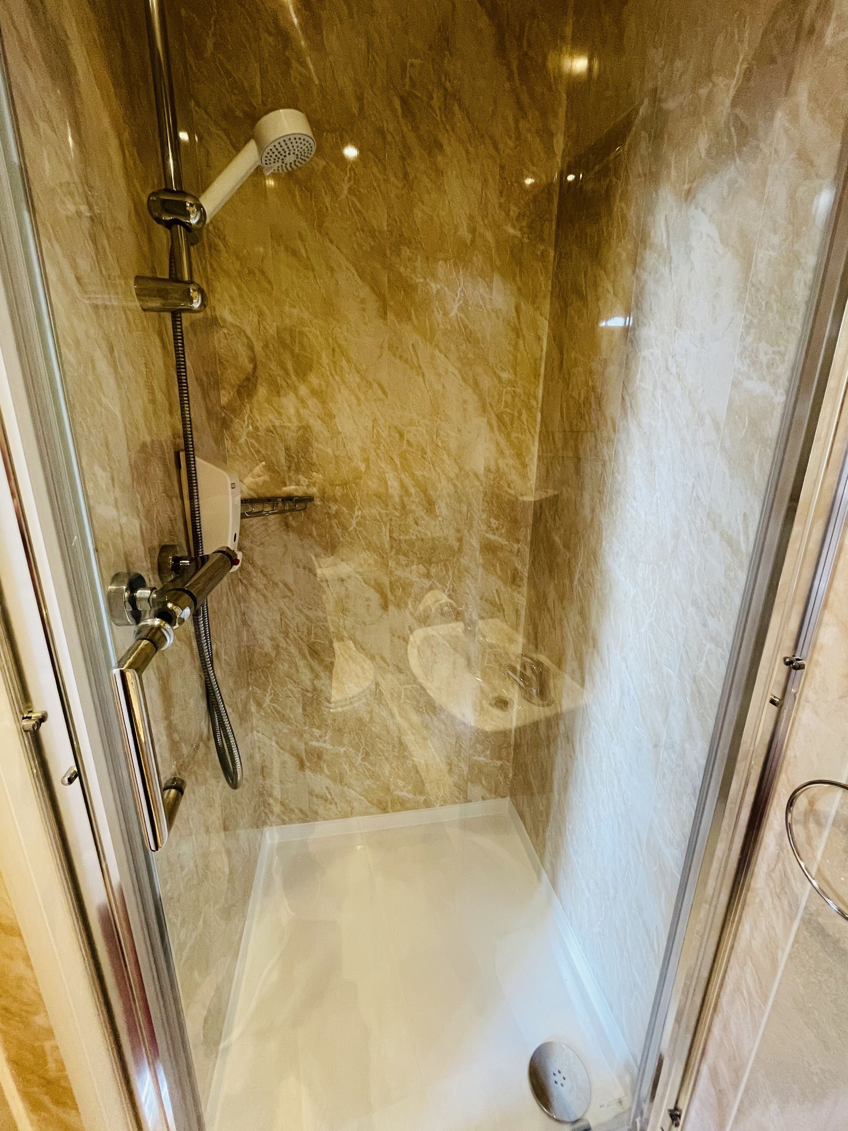 Une douche fermée par des parois en verre, dotée d’un pommeau de douche à main, d’un robinet mural et d’un panneau de commande.
