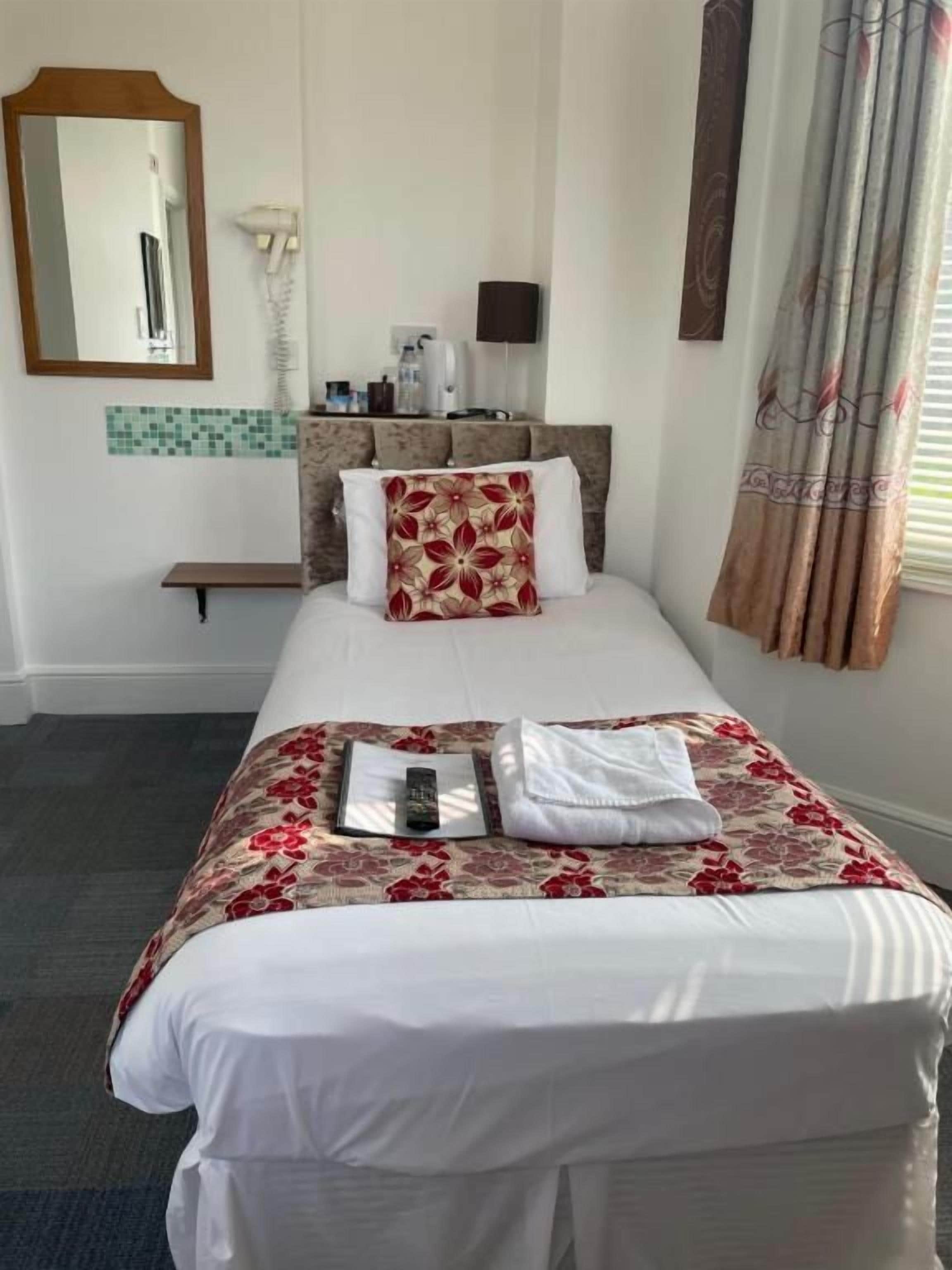 A hotel room with a bed, a bedside table, a mirror, a telephone, and a window with curtains.
