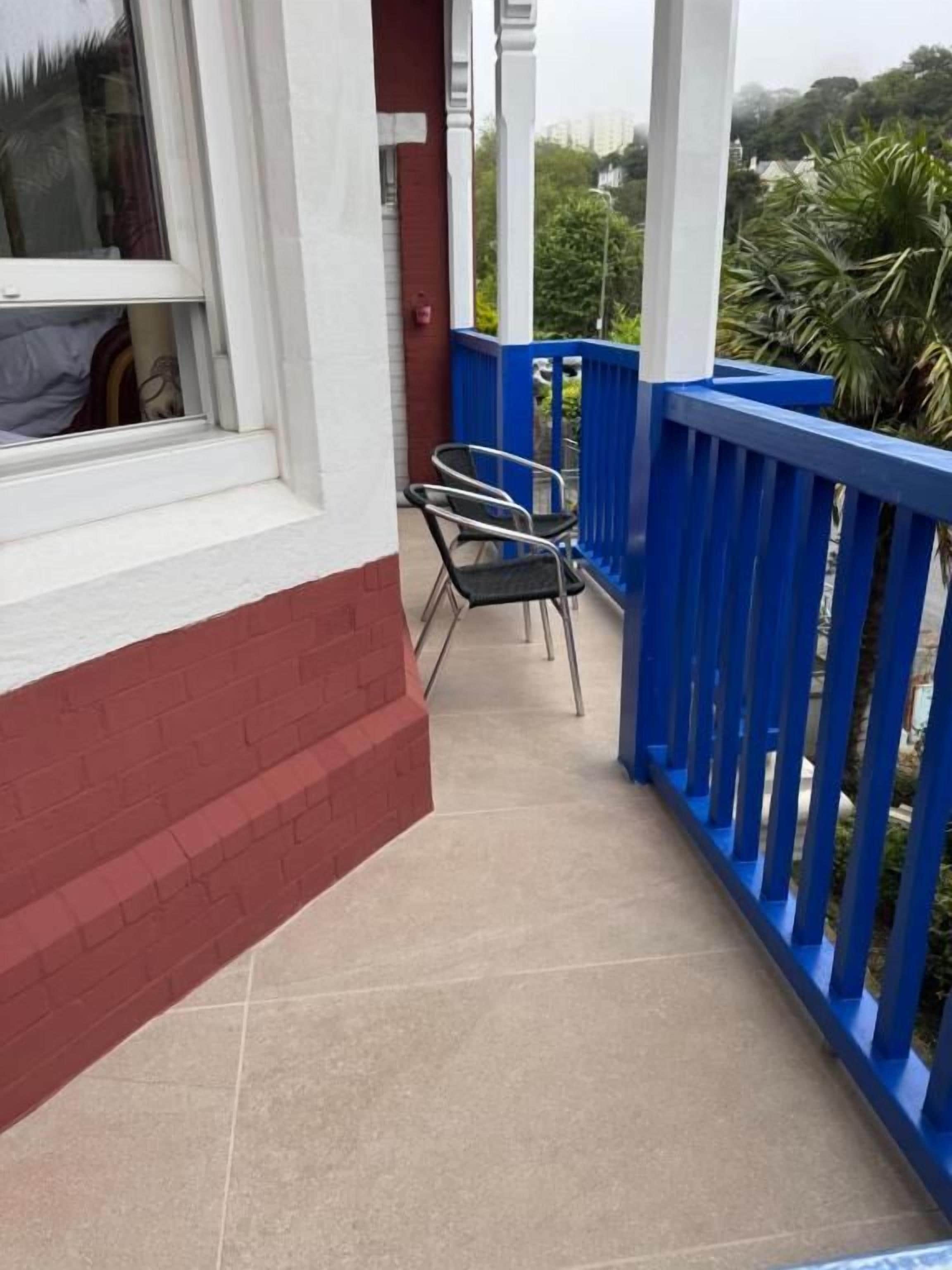 A balcony with a blue railing, a window, and a chair.