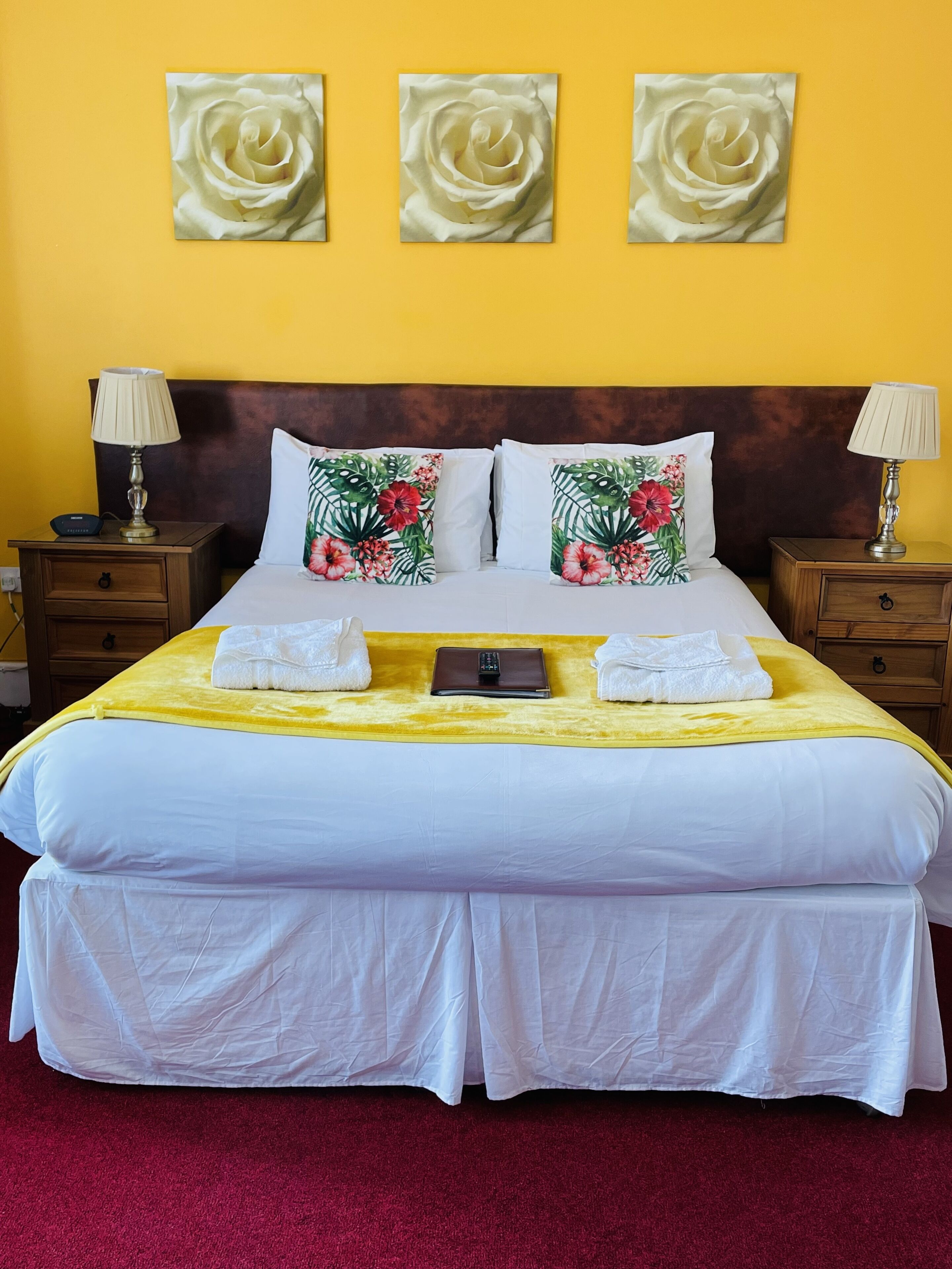 Une chambre d’hôtel avec un grand lit, deux tables de chevet, une tête de lit et trois tableaux représentant des roses, accrochés au mur.