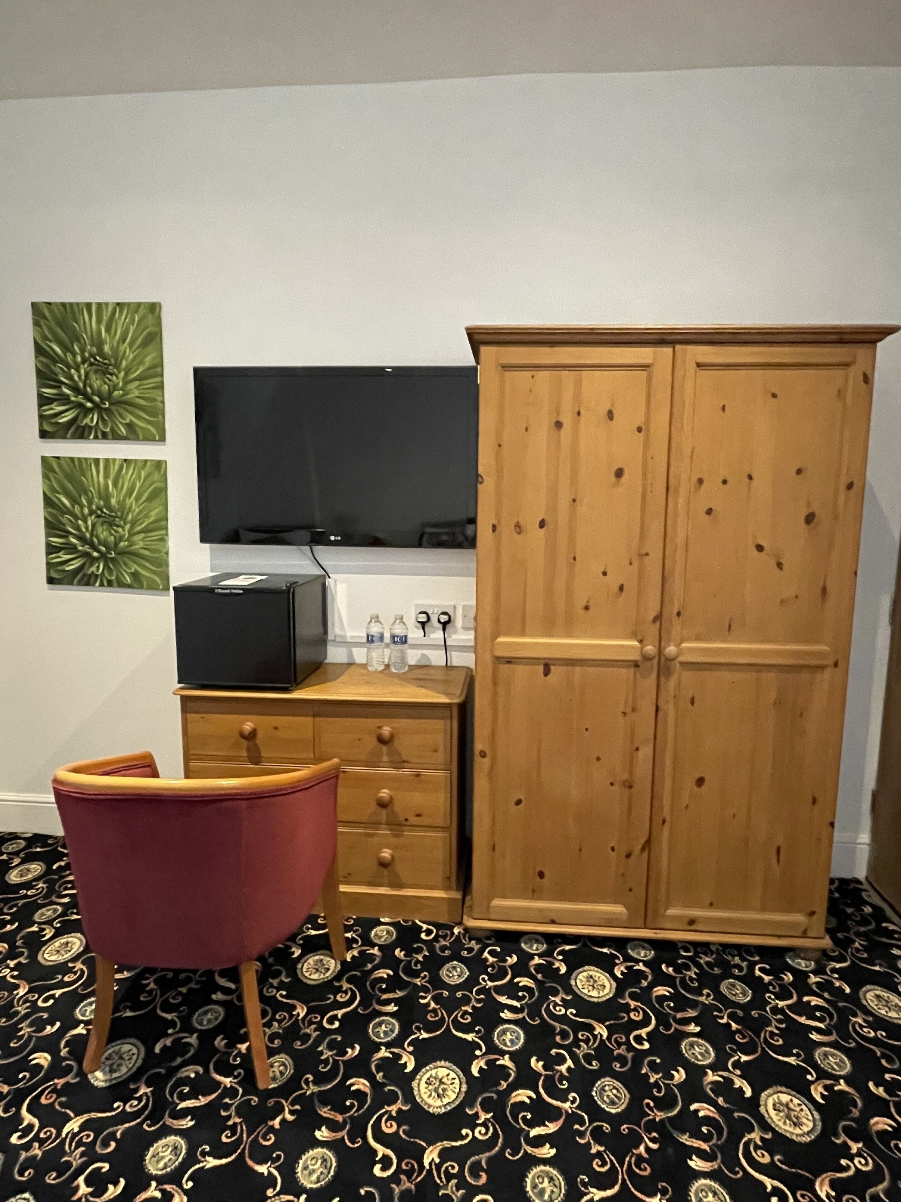 Habitación con armario de madera, una silla roja, un televisor de pantalla plana y alfombra estampada.