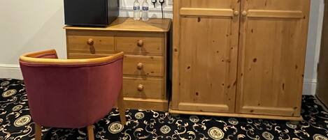 Habitación con armario de madera, una silla roja, un televisor de pantalla plana y alfombra estampada.
