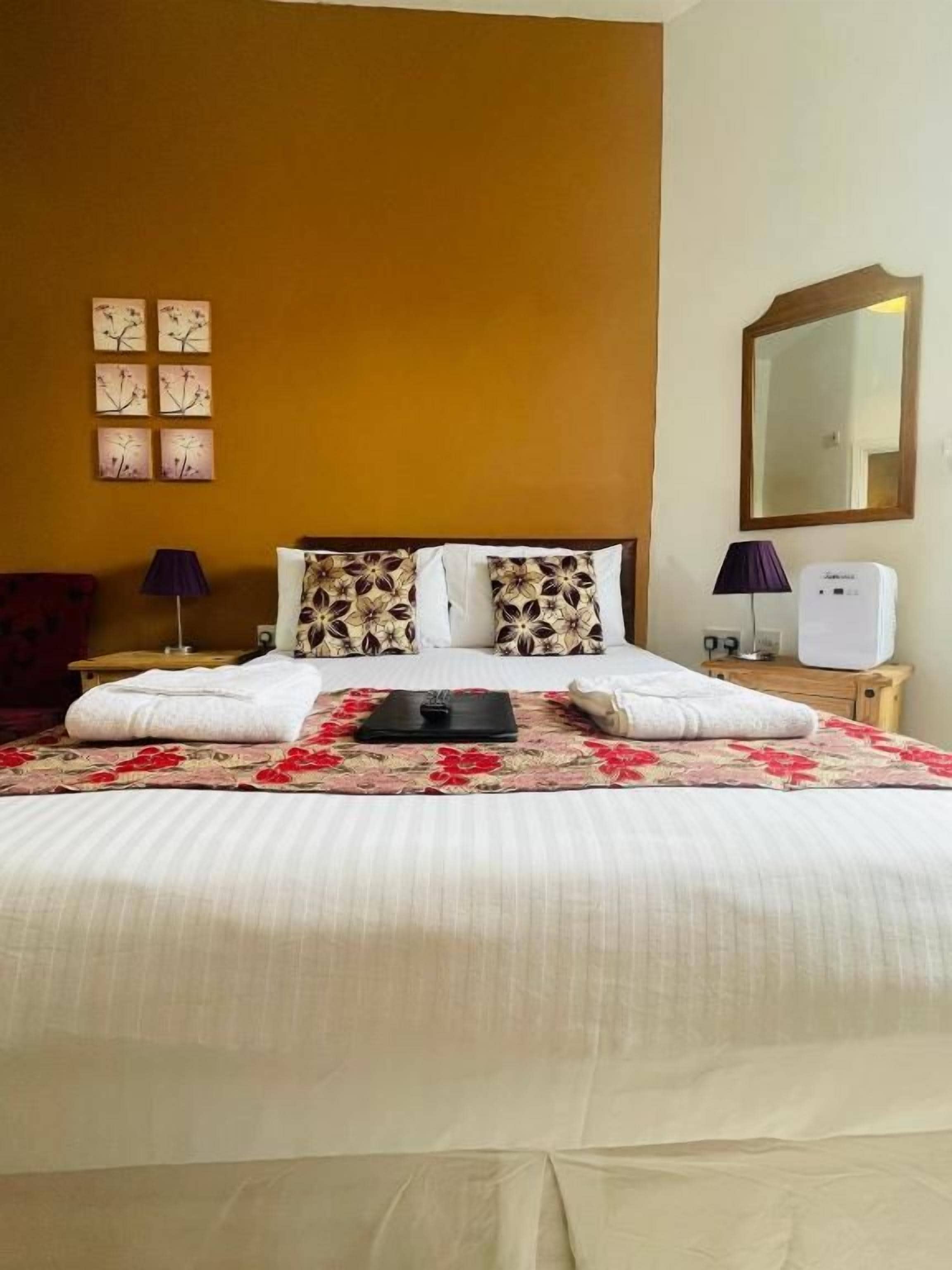 A hotel room with a large bed, a bedside table, a lamp, a mirror, and wall art.