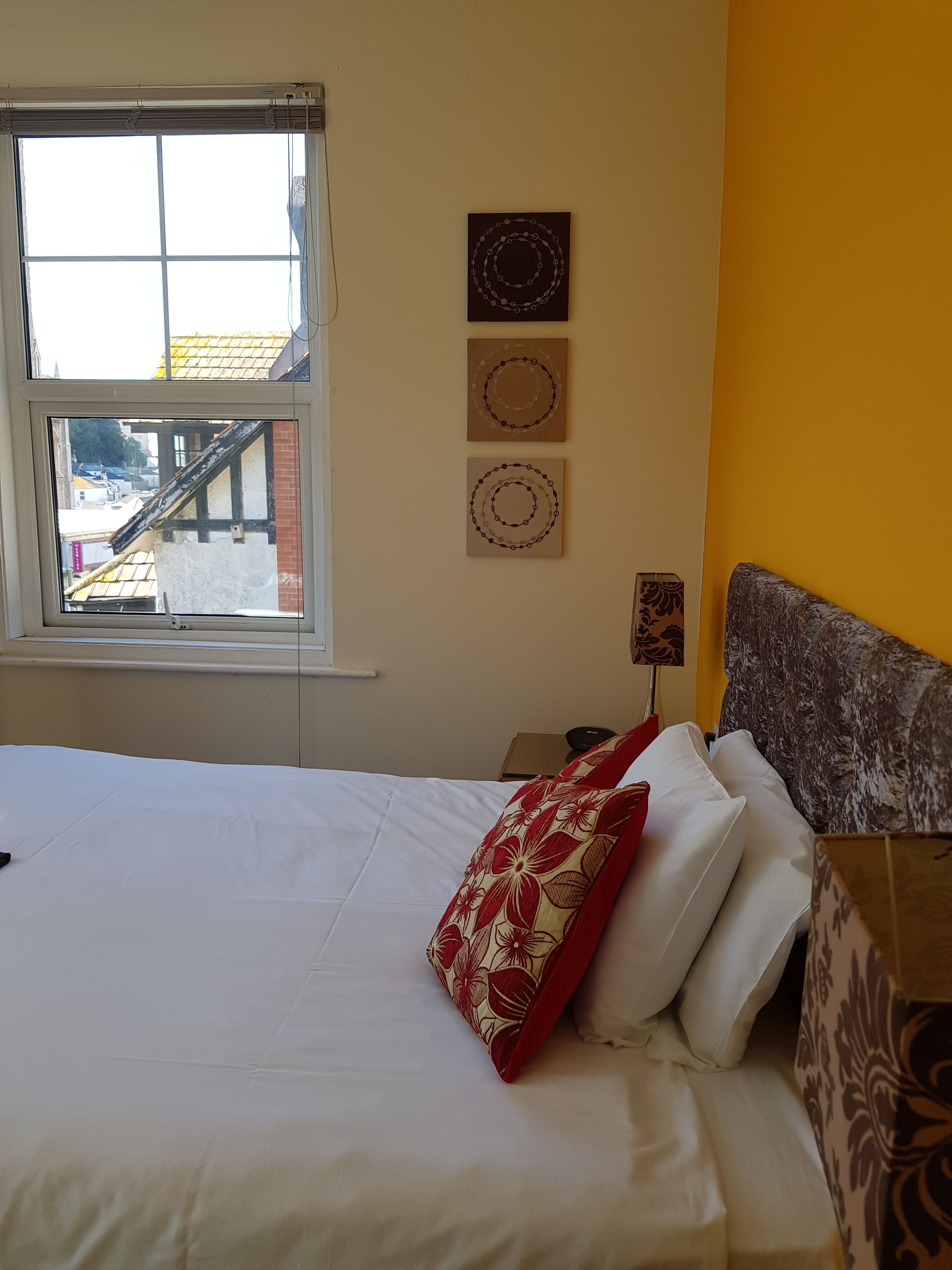 A hotel room with a bed, a nightstand, a lamp, and a window with a view of buildings outside.
