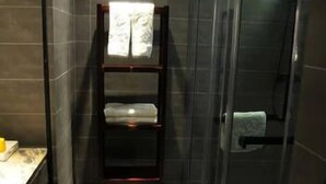 A bathroom with a glass shower enclosure, a dark tiled wall, and a wooden shelf with towels. - Chenxi Fengqing Hotel (Zhaoqing)