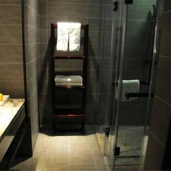 A bathroom with a glass shower enclosure, a dark tiled wall, and a wooden shelf with towels. - Chenxi Fengqing Hotel (Zhaoqing)