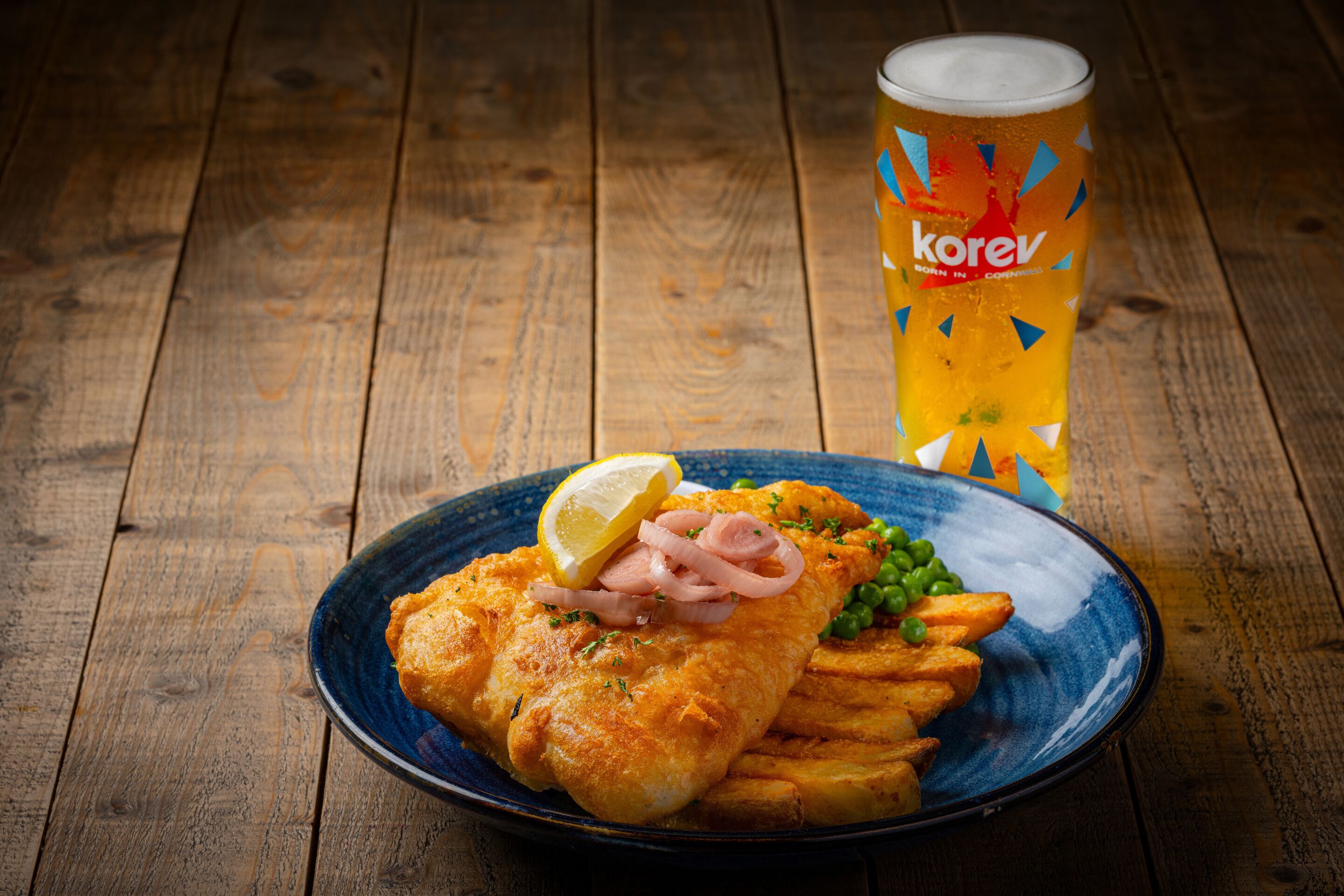 Um prato de peixe com batatas fritas e um copo de cerveja sobre uma mesa de madeira.