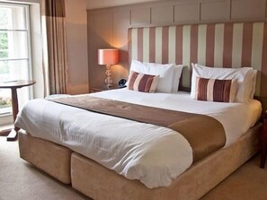 A large bed with a striped headboard, a bedside lamp, and a view of the outdoors through a window.