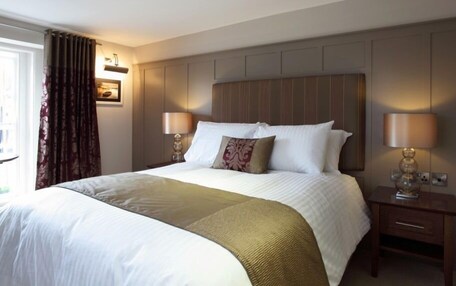 Una habitación de hotel con una cama grande, dos mesitas de noche con lámparas, una ventana con cortinas y un aplique de pared.