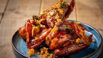 A plate of glazed and fried chicken wings garnished with herbs.