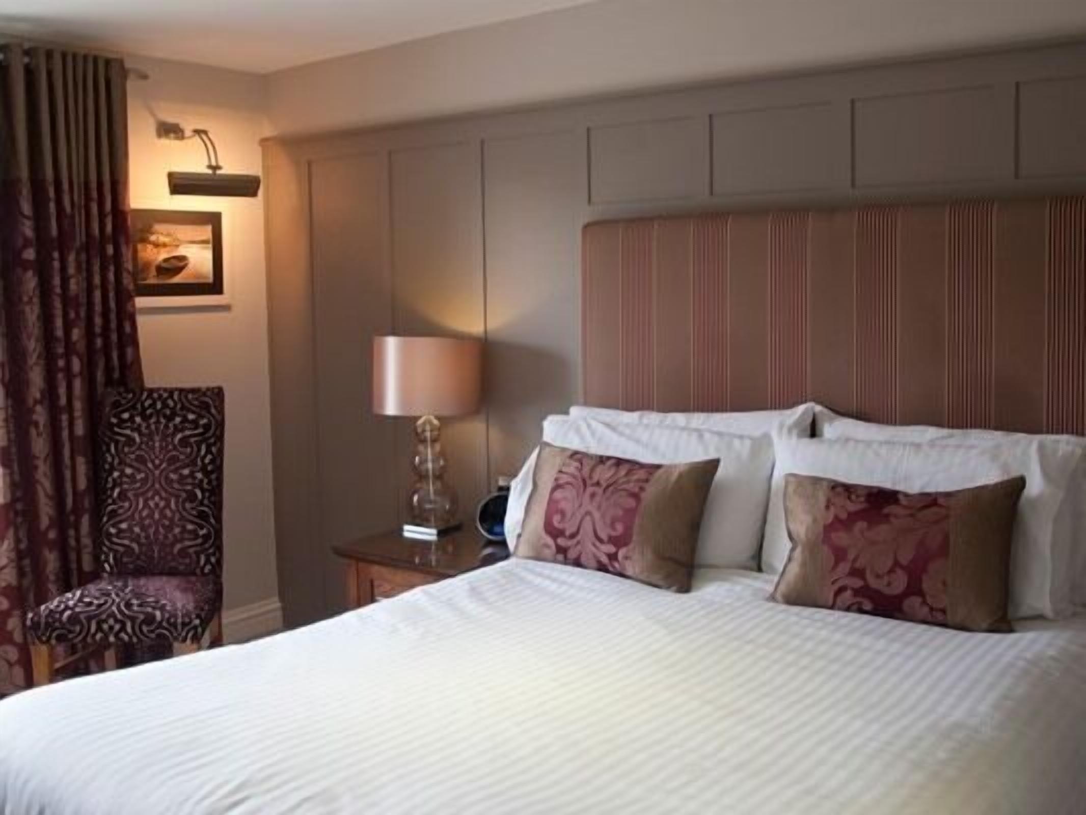 A hotel room with a large bed, a nightstand with a lamp, a chair, and a wall-mounted picture.