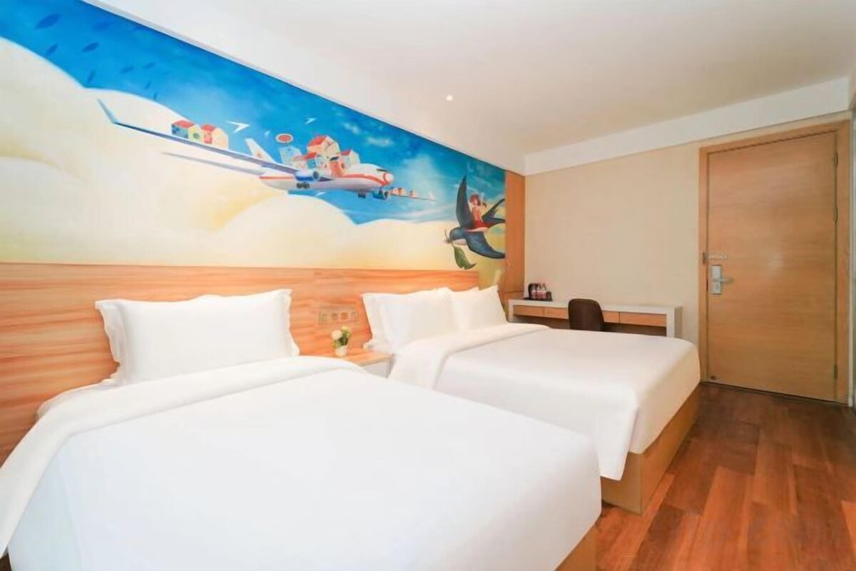A hotel room with two beds, a wooden headboard, a mural on the wall, and a wooden door.