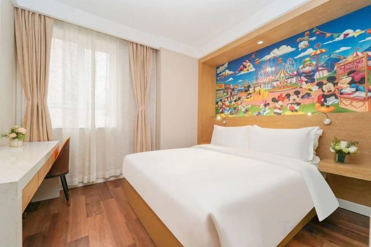 A hotel room with a bed, a desk, and a mural on the wall.