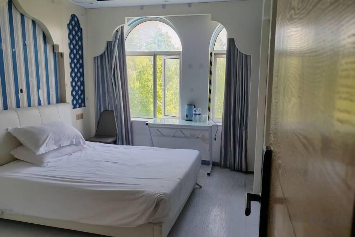 A hotel room with a bed, desk, and large window.