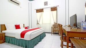 Habitación de hotel con cama, escritorio, silla, aire acondicionado, ventana con cortinas y televisor.