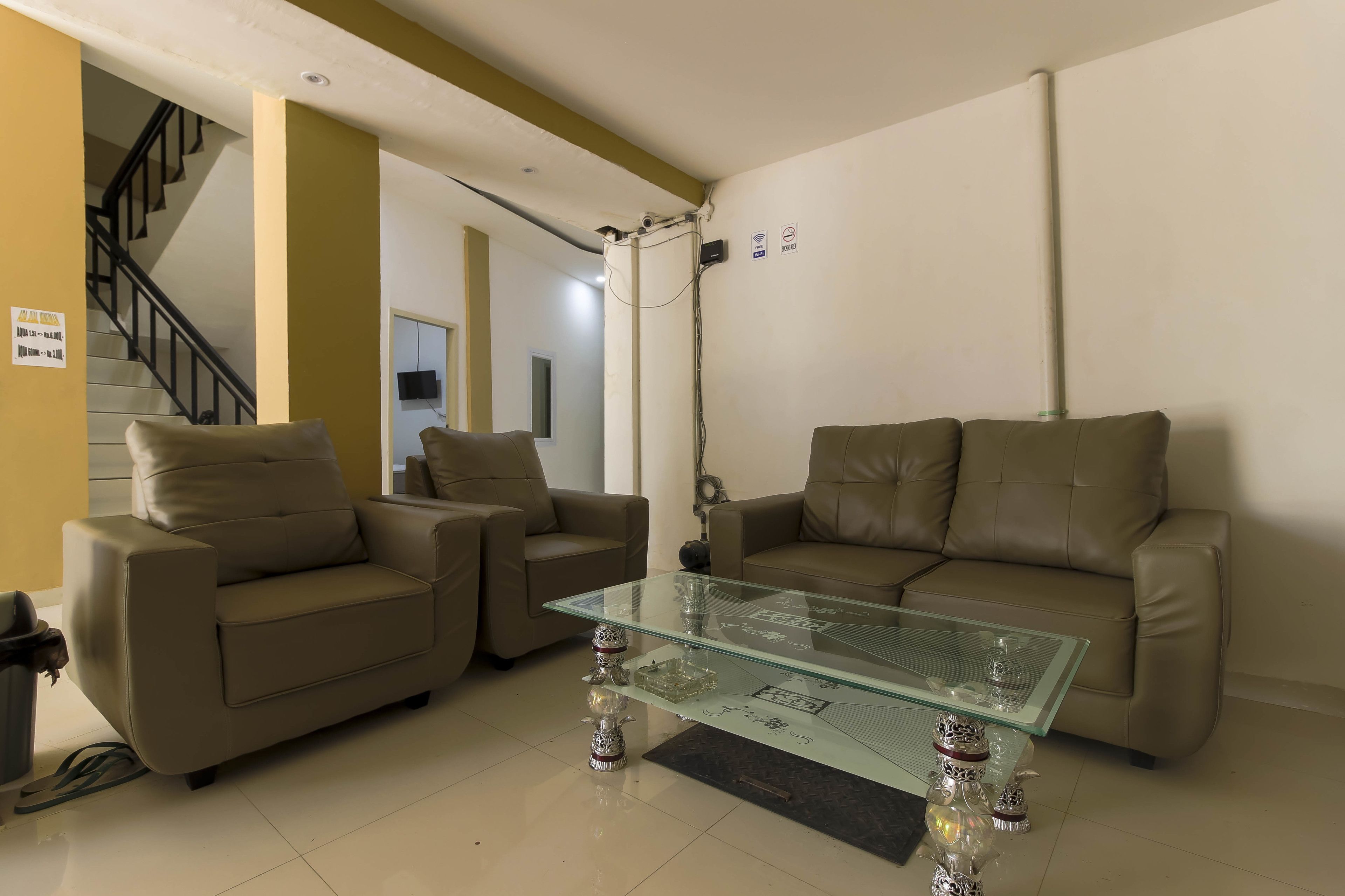 Una sala de estar con dos sofás beige, una mesa de centro de vidrio y una escalera al fondo.