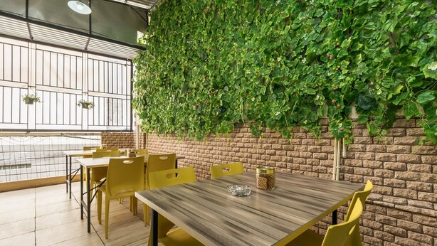 A dining area with yellow chairs and tables, a brick wall, and a green ivy-covered wall. - RedDoorz near Palembang Trade Center (Palembang)
