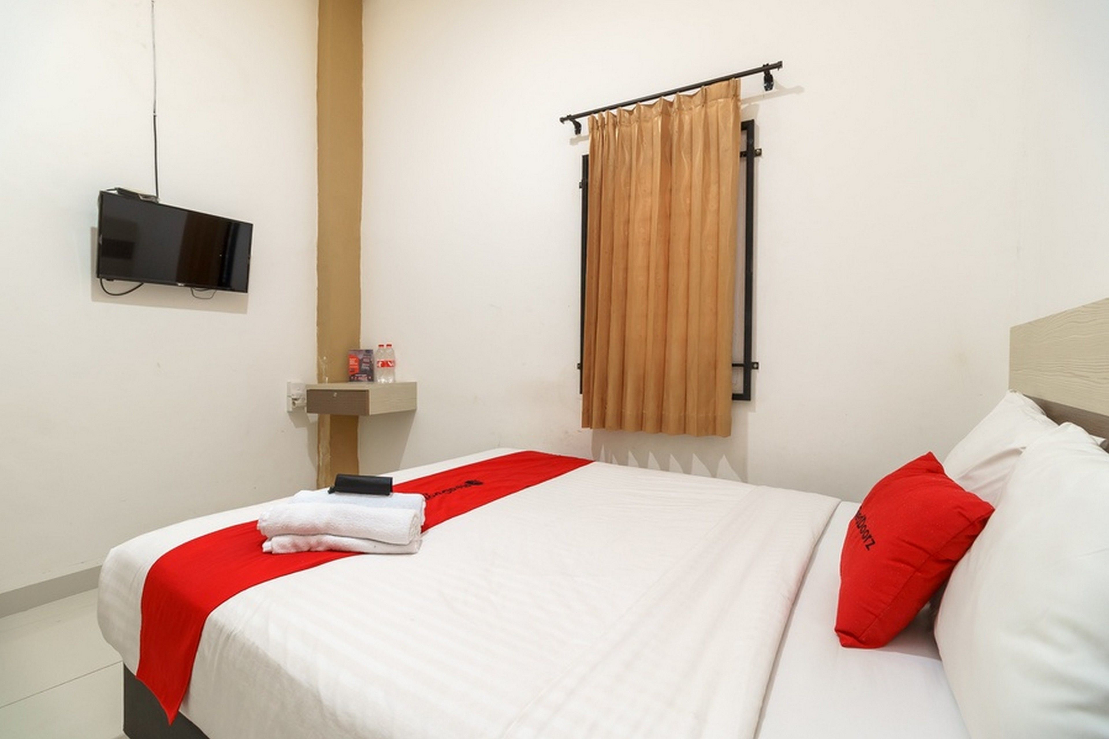 A hotel room with a bed, a TV mounted on the wall, a bathroom with a sink, and a window with curtains.