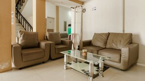 A living room with two beige sofas, a glass coffee table, and a staircase in the background. - RedDoorz near Palembang Trade Center (Palembang)