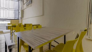 A conference room with a large table and yellow chairs, equipped with electrical outlets and a window with metal bars. - RedDoorz near Palembang Trade Center (Palembang)
