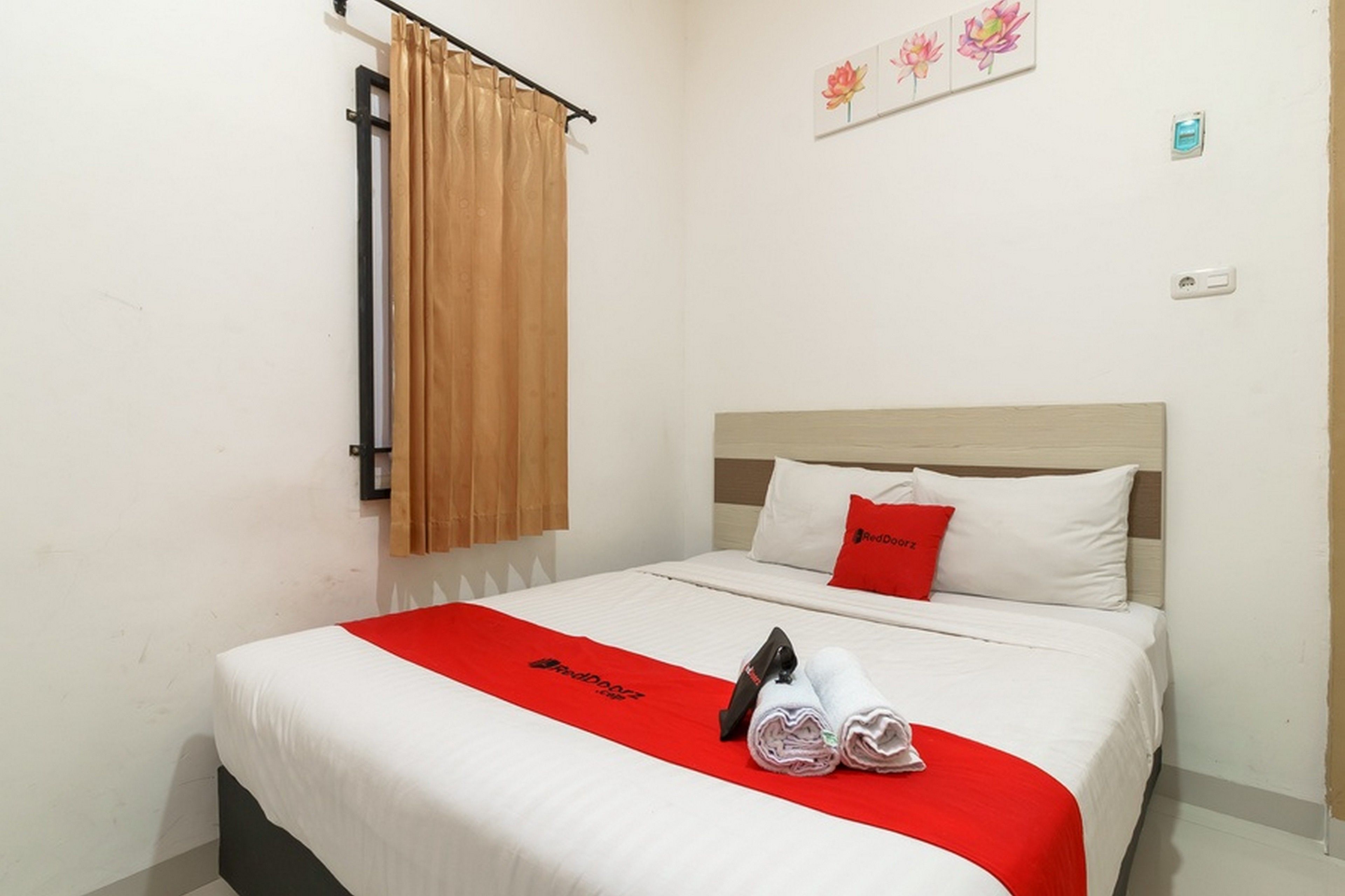 A hotel room with a bed, a red blanket, a pillow, and a towel.