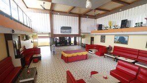 A spacious indoor area with red seating, a central table, and a television mounted on the wall. - RedDoorz Plus near DC Mall Batam (Batam)