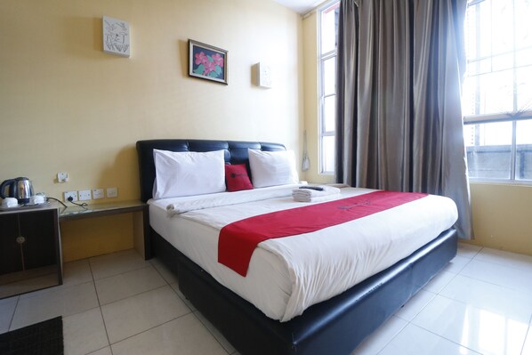 A hotel room with a bed, a bedside table with a kettle, a power outlet, and a window with curtains. - RedDoorz Plus near DC Mall Batam (Batam)