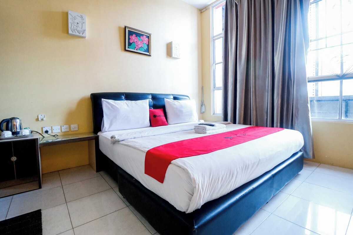 A hotel room with a bed, a nightstand, a window with curtains, and a wall with two framed pictures.