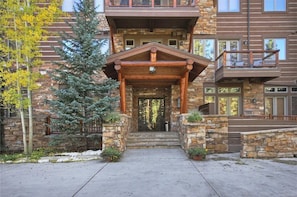 A multi-story building with a stone facade, a wooden porch, and a staircase leading to the entrance. - Keystone Village Condos by Gondola Resorts (Keystone)
