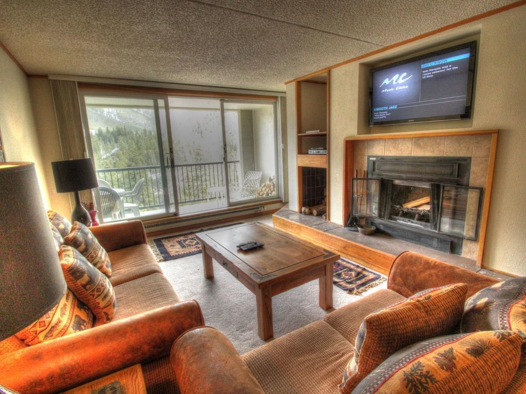 Ein Wohnzimmer mit Kamin, Fernseher und einem großen Fenster mit Blick auf Bäume.
