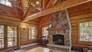 L’intérieur d’une cabane en rondins, avec une cheminée en pierre, des meubles en bois et de grandes fenêtres.