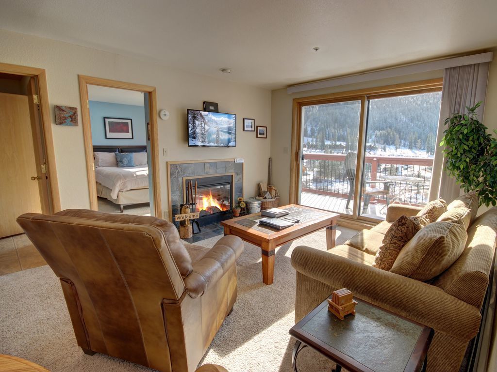 A cozy living room with a fireplace, comfortable seating, and a large window offering a view of a snowy landscape.