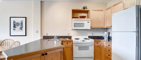 A kitchen with wooden cabinets, a white stove, a microwave, and a refrigerator.