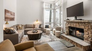 A modern living room with a stone fireplace, a large flat-screen TV, and a cozy seating area. - Downtown Aspen Vacation Rentals (Aspen)