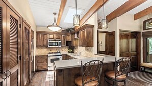 A kitchen with wooden cabinets, a central island, bar stools, and pendant lighting. - Downtown Aspen Vacation Rentals (Aspen)