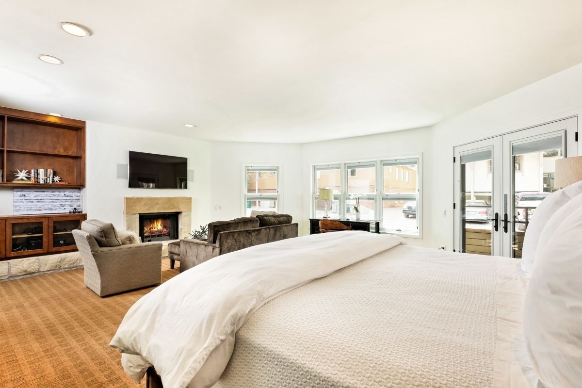 A spacious bedroom with a large bed, a fireplace, a seating area, and a view of the outside.