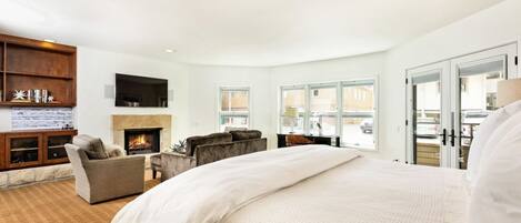 A spacious bedroom with a large bed, a fireplace, a seating area, and a view of the outside.