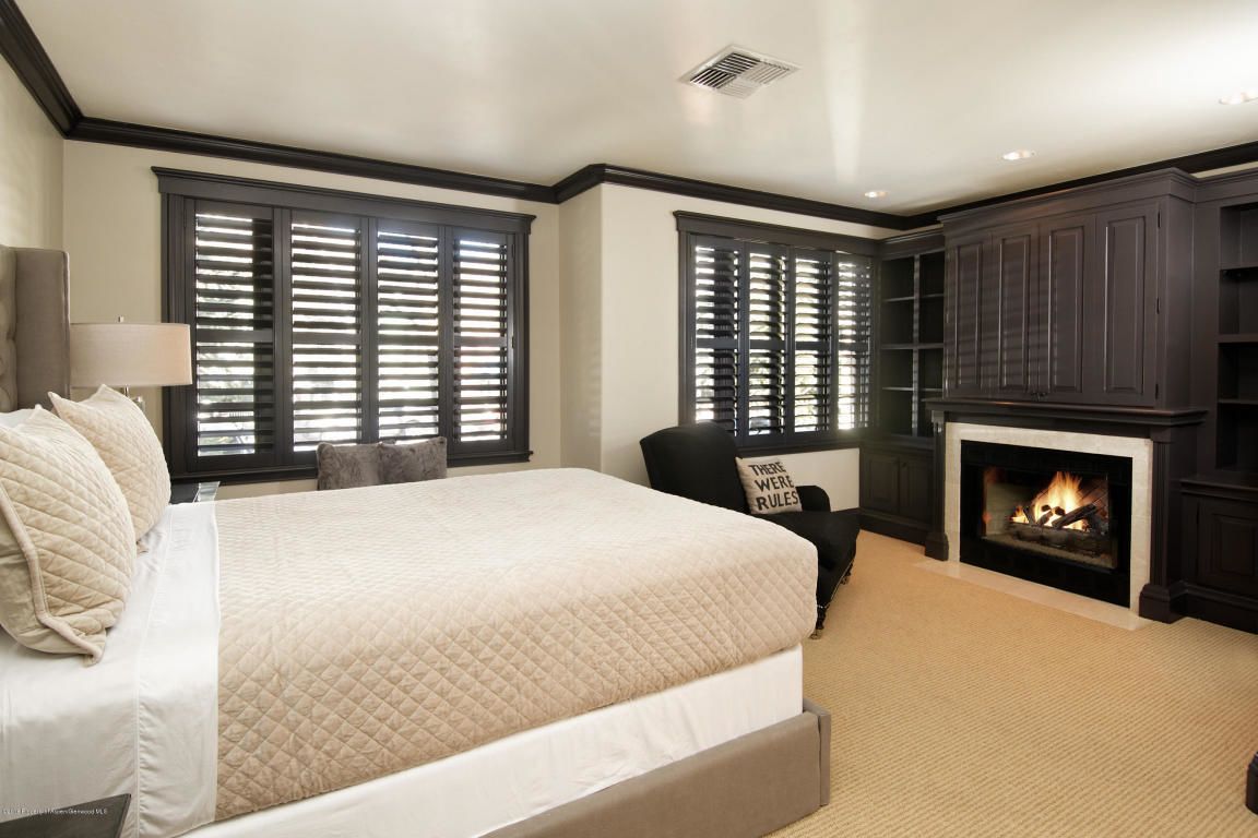 A bedroom with a large bed, a fireplace, and two windows with blinds.