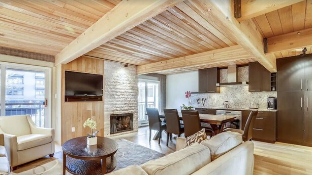 A spacious living area with a fireplace, a dining table, and a kitchen with dark cabinets. - Downtown Aspen Vacation Rentals (Aspen)