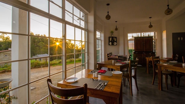 A spacious dining area with large windows, wooden tables, and chairs. - Misthill Rest (Nuwara Eliya)