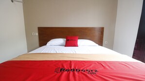 Sängyssä on puinen pääty, valkoiset vuodevaatteet ja punainen tyyny, jossa on RedDoorz-logon kuvio.