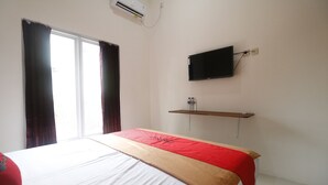 Hotellihuone, jossa on sänky, seinälle asennettu televisio ja ikkuna, jossa on verhot.