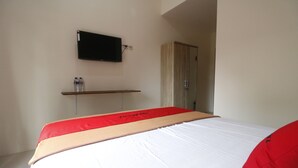 Hotellihuone, jossa on sänky, seinälle asennettu televisio, vaatekaappi ja hylly, jossa on vesipulloja.