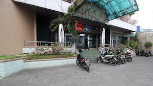 A hotel entrance with a sign, a palm tree, and several parked motorcycles. - Akur Hotel Malioboro (Yogyakarta)