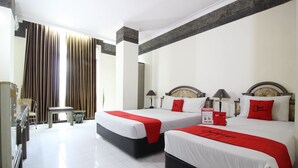 A hotel room with two beds, a small table, a chair, and a view of the outside through large curtains. - Akur Hotel Malioboro (Yogyakarta)