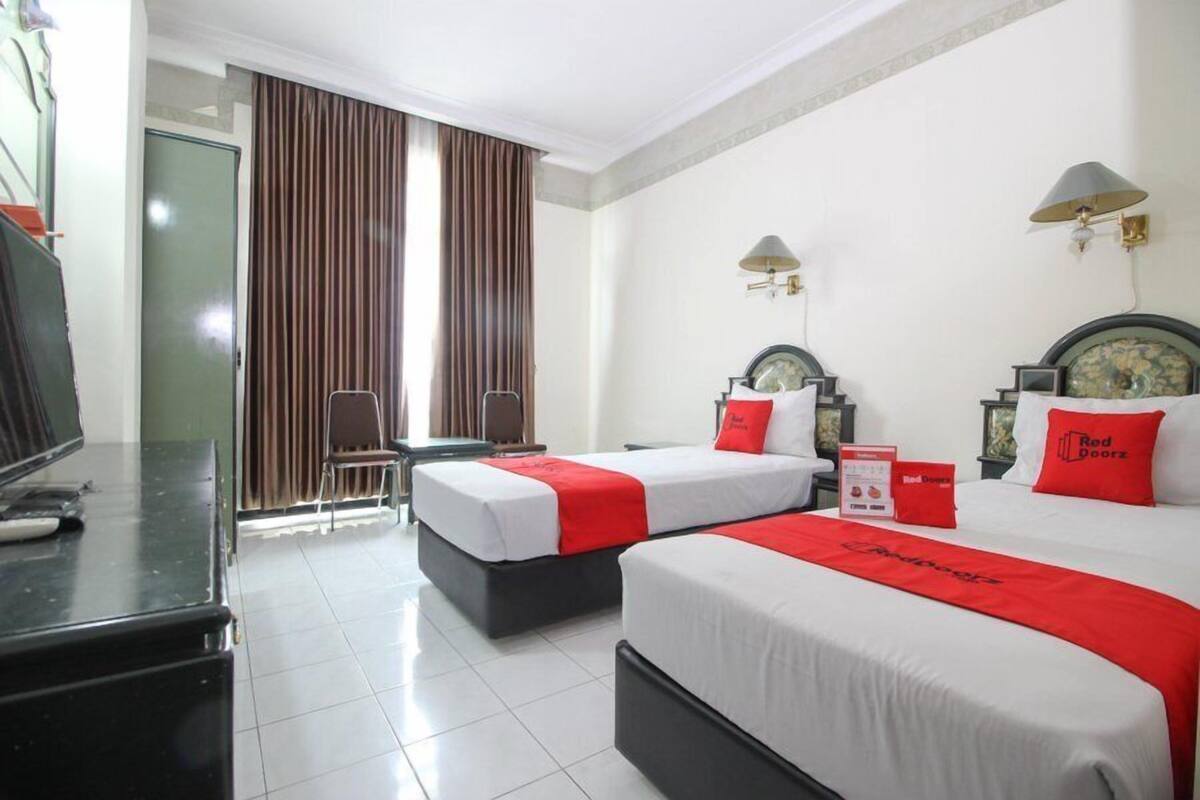 Quarto de hotel com duas camas, uma escrivaninha, televisão e janela com cortinas.
