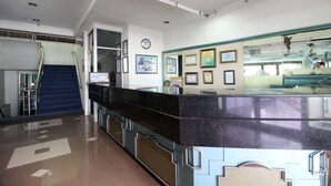 A reception area with a black marble counter, framed certificates on the wall, and a staircase leading to an upper floor. - Akur Hotel Malioboro (Yogyakarta)