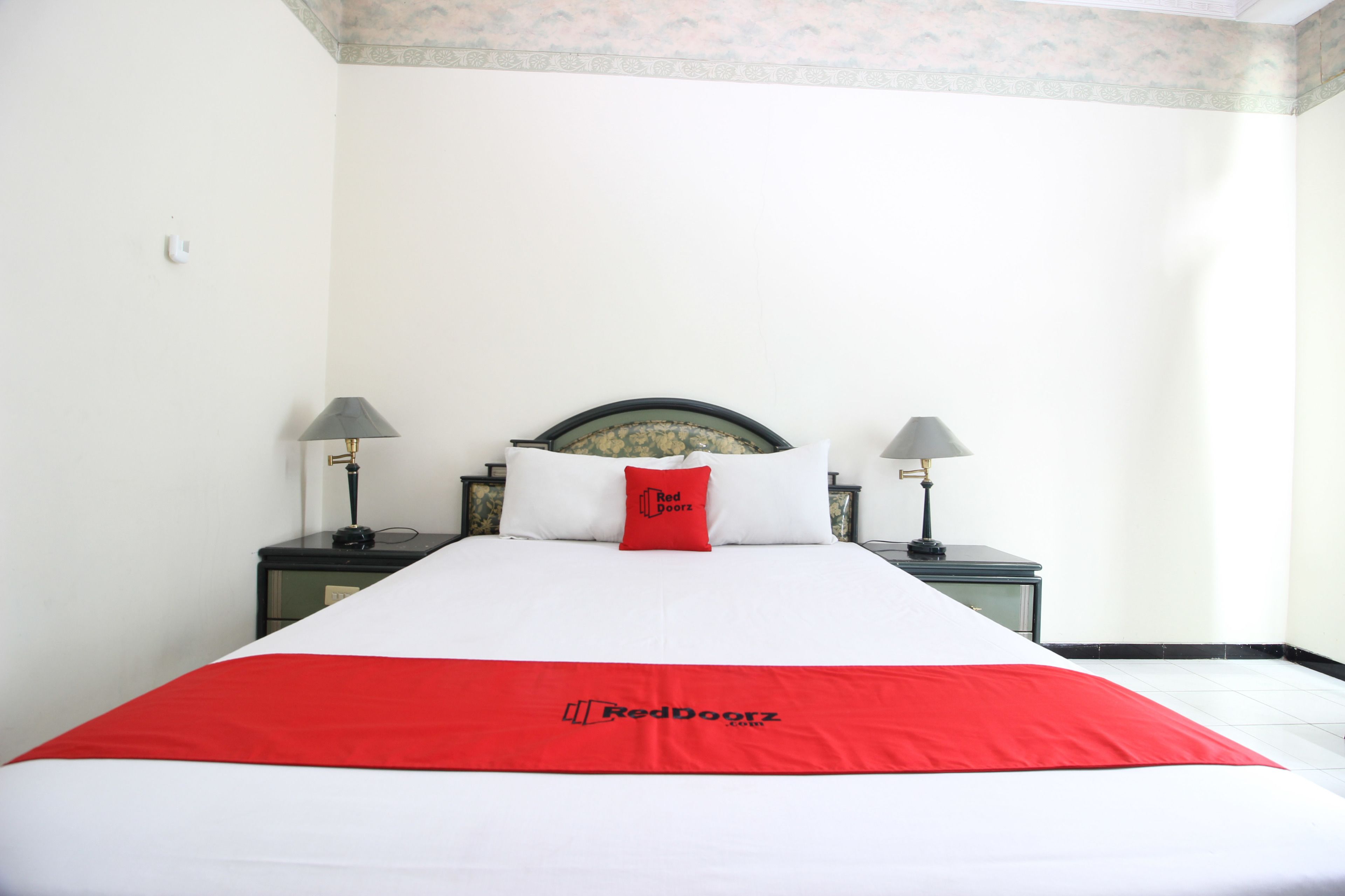 A neatly made bed with a red and white bedspread, two bedside lamps, and a headboard with a floral pattern.