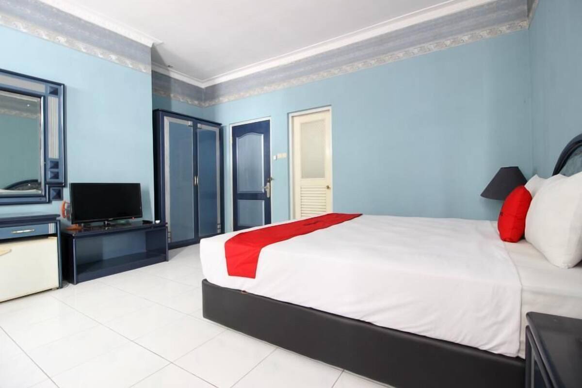 Quarto de hotel com uma cama, televisão, escrivaninha e guarda-roupa.